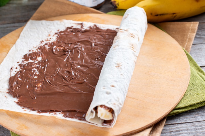 banana being rolled tightly inside crepe with chocolate spread