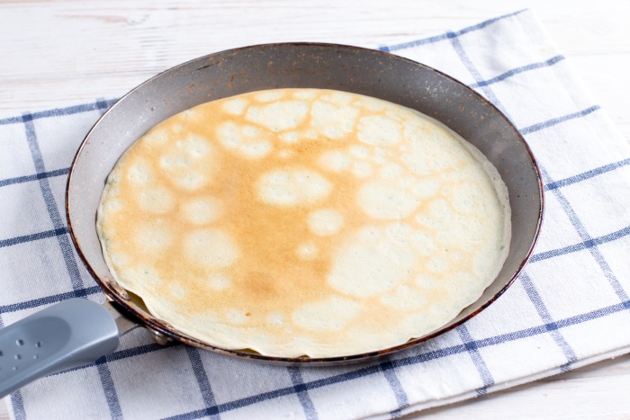 thin crepe in pan with light golden edges ready to make banana nutella crepe rolls